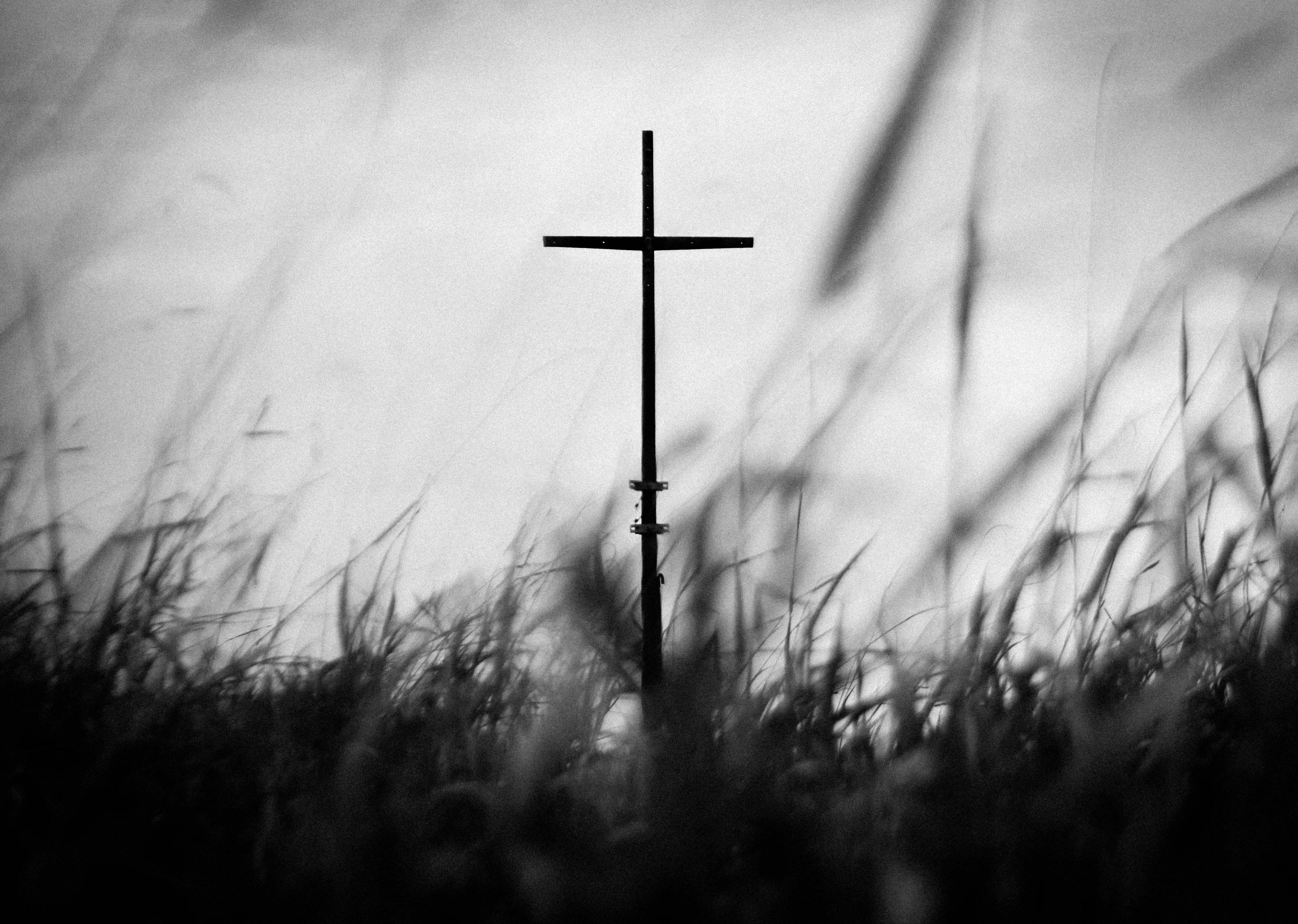 Silhouette of a cross against a cloudy sky with grass in the foreground